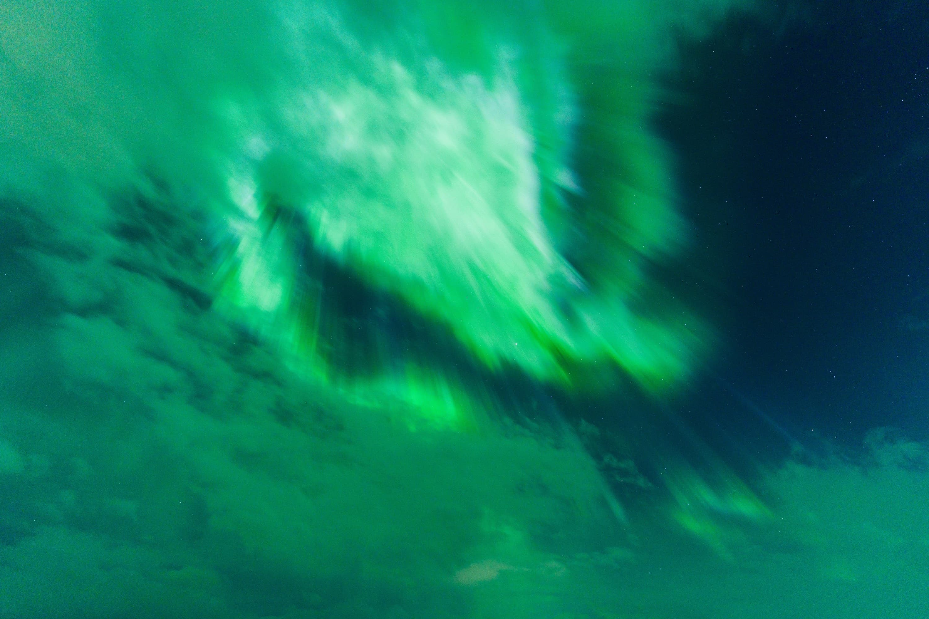 Emerald aurora curling through clouds against a deep blue night sky.