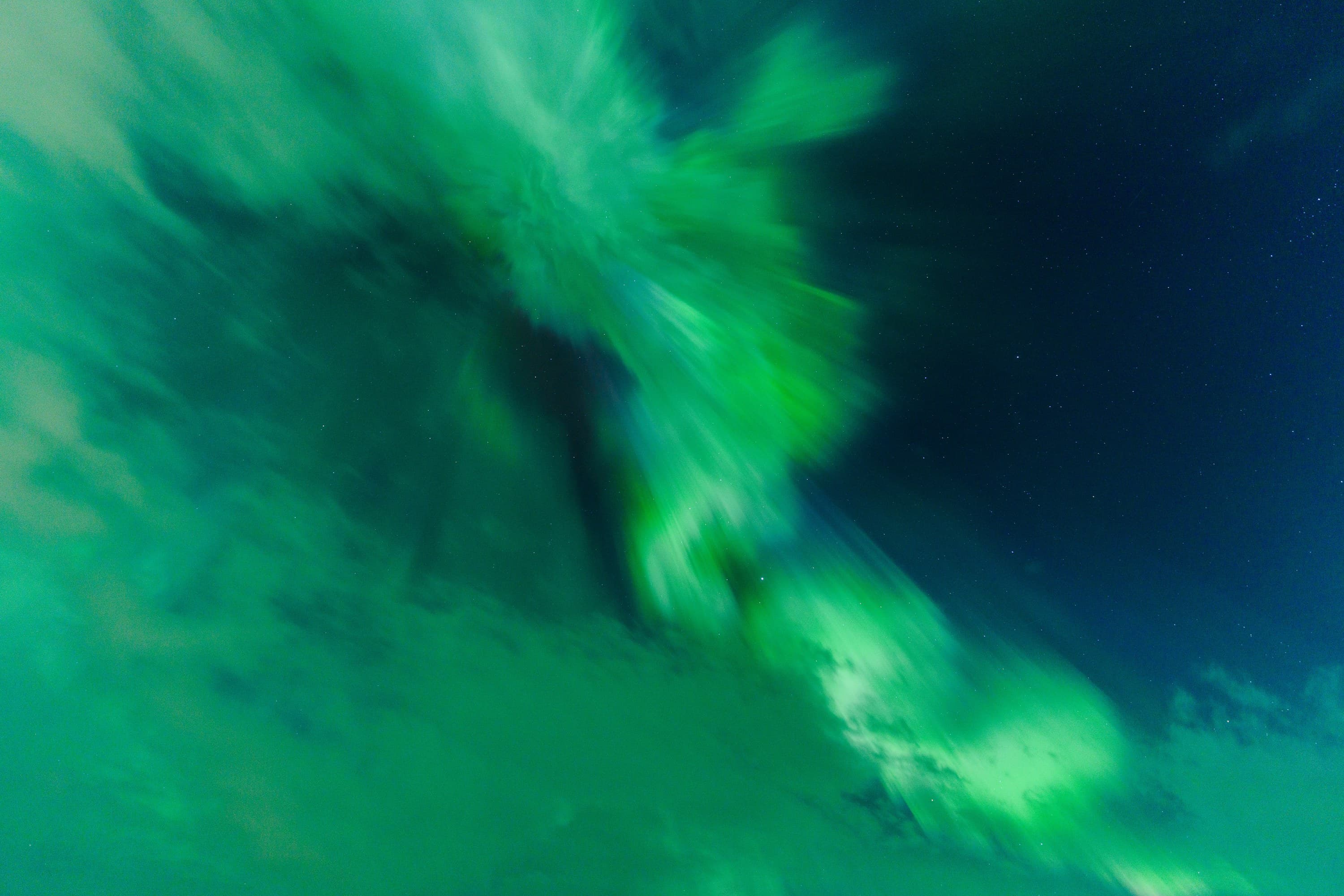A flowing green aurora folding diagonally across a dark blue opening in the clouds.