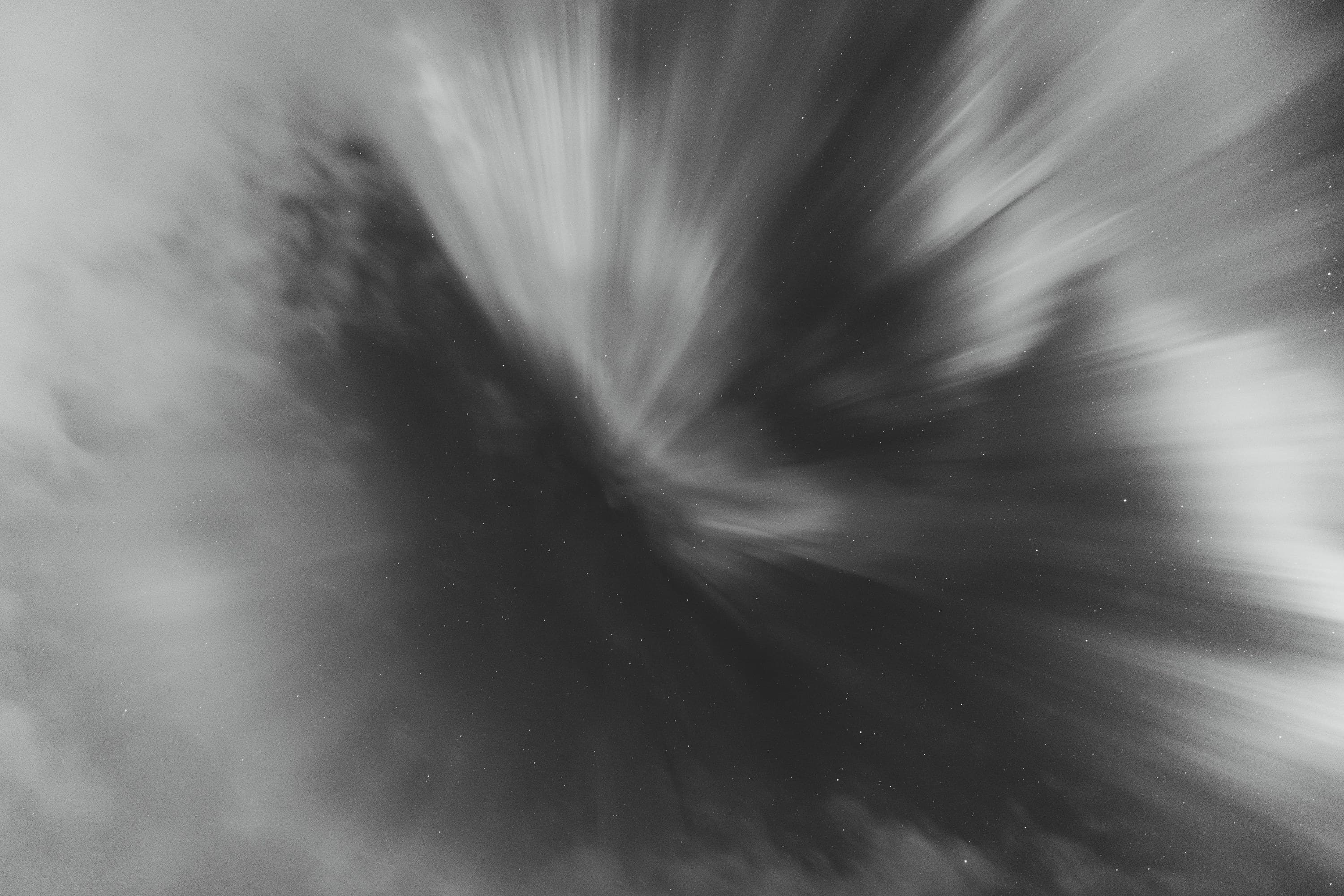 Black-and-white aurora bursting outward in soft, luminous streaks.