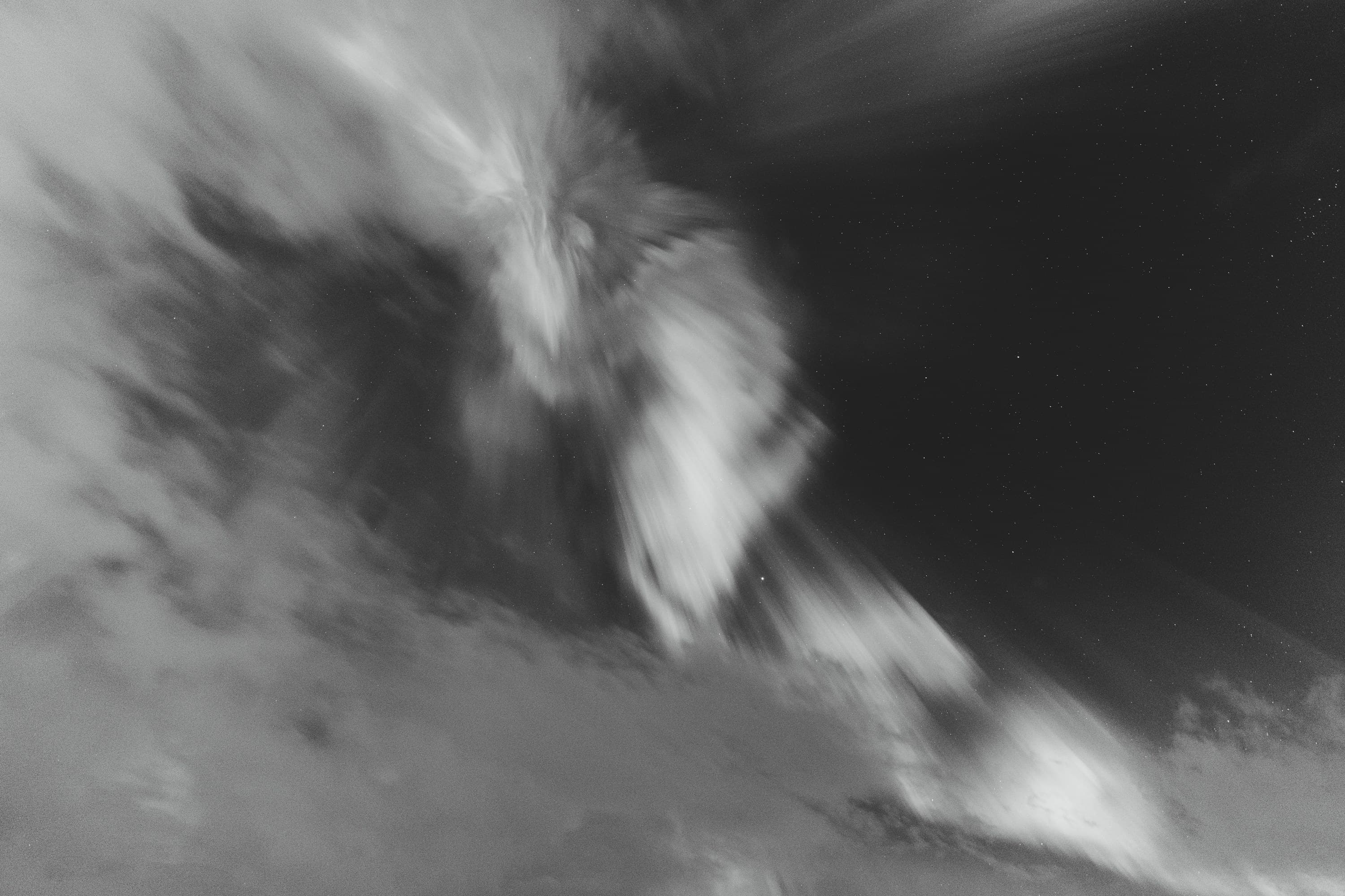 Black-and-white aurora curling like a wave beneath a field of stars.