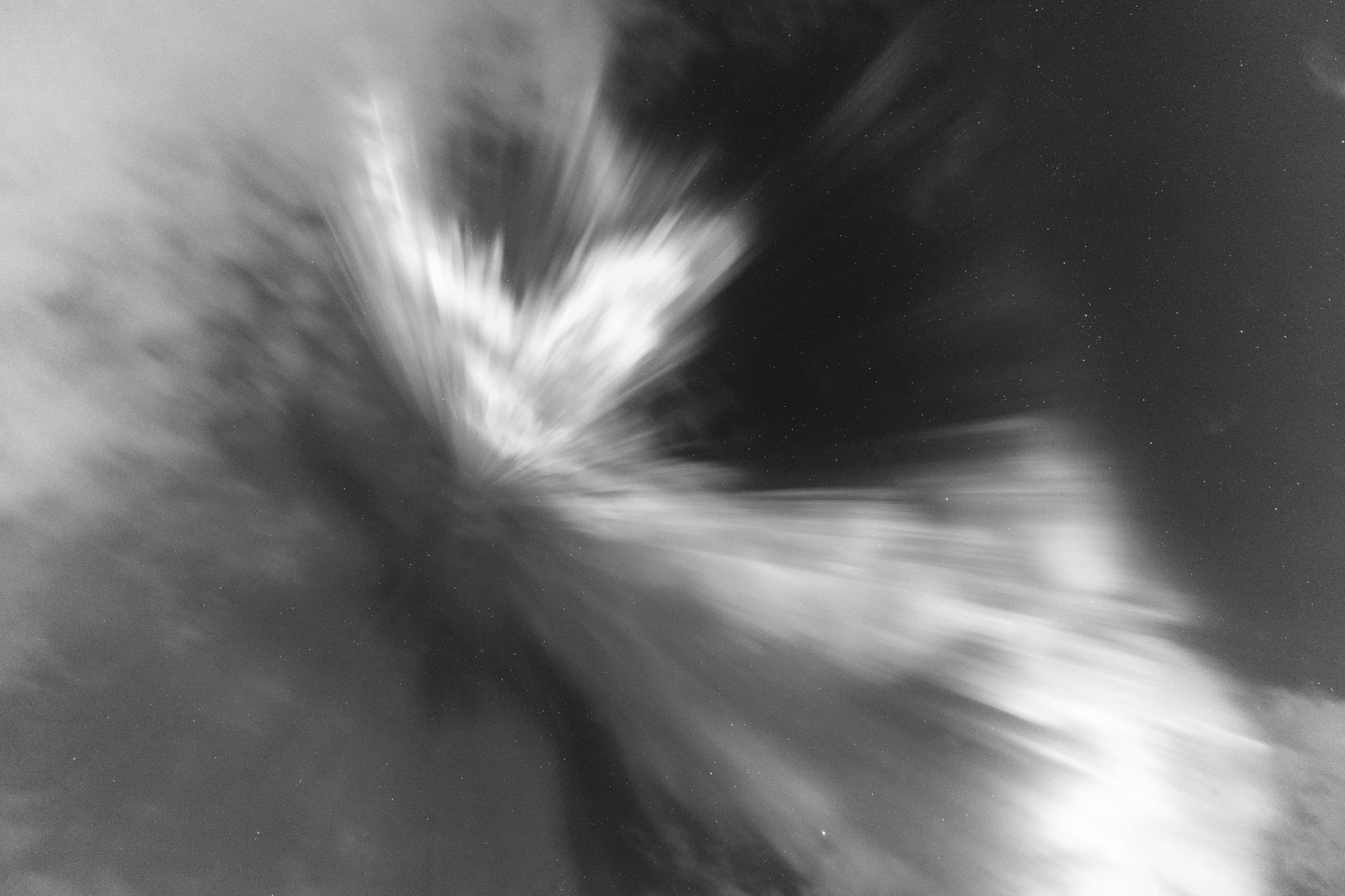 Luminous black-and-white aurora sweeping through clouds in a broad spiral.