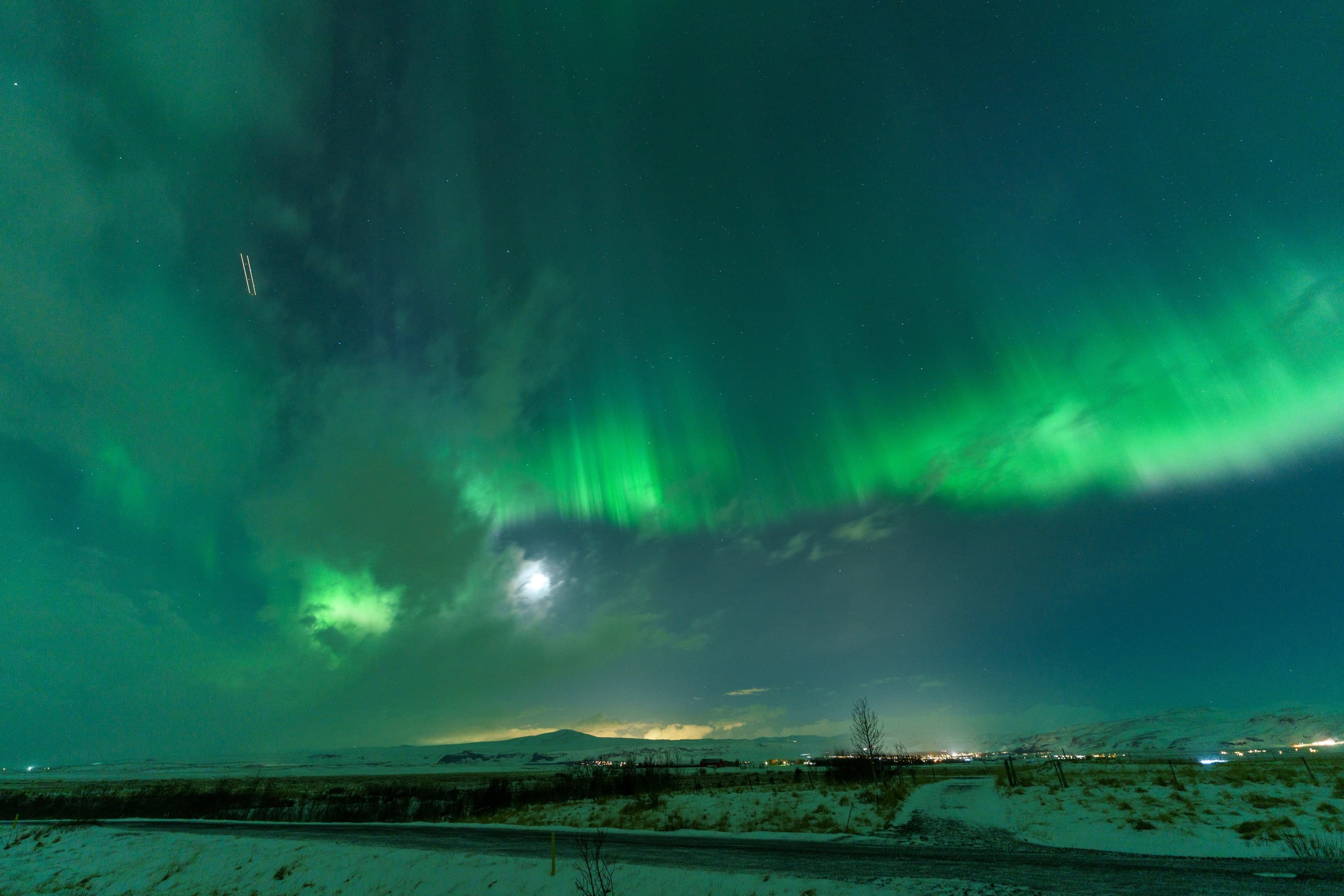 Green aurora and a bright moon hanging above a snow-covered Icelandic landscape.